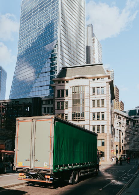 A large green cargo truck with closed rear doors is parked on a city street during daylight hours, ready for home relocation or furniture transport as part of a professional removals service by Kilbur
